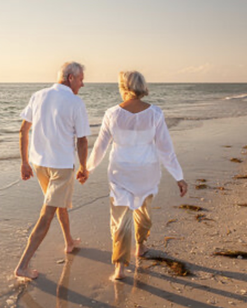 Elderly couple walking hand-in-hand on a serene beach at sunset, symbolizing wellness, bonding, and vitality
